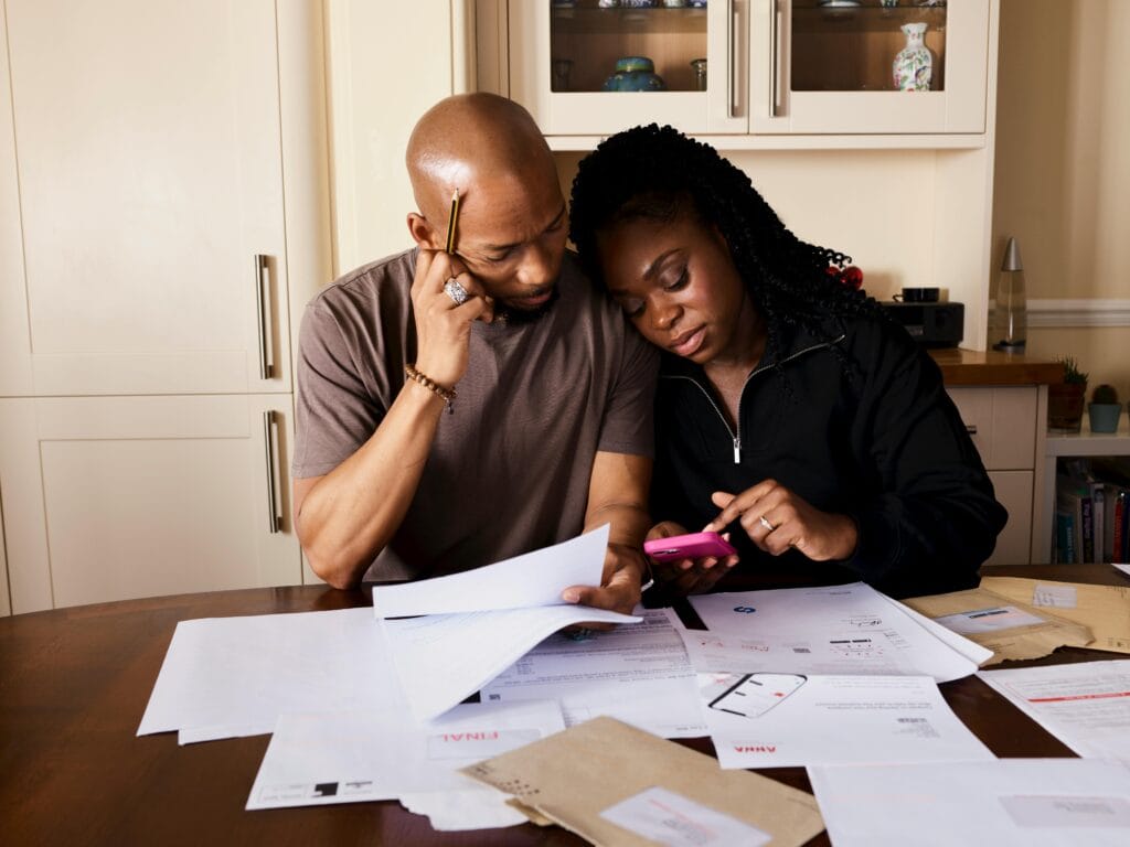 pexels-photo-14599250-14599250 A couple sits at a table managing domestic finances, evaluating documents and using a smartphone.