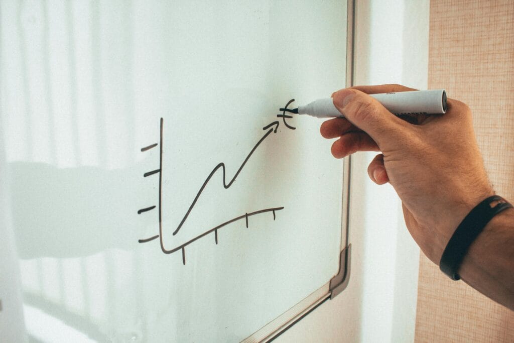 A hand draws an upward graph with a euro symbol on a whiteboard, depicting financial growth.
